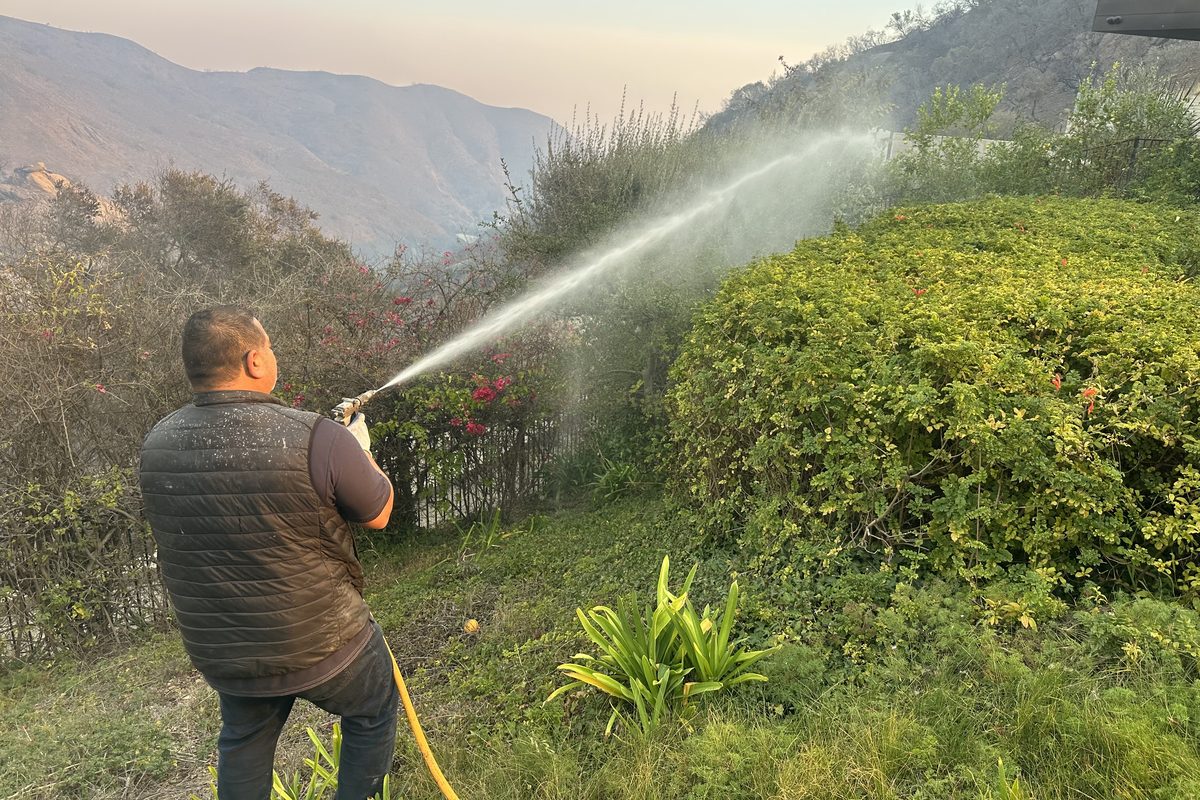 An Allied applicator spraying long-term fire retardant onto hillside vegetation above a property