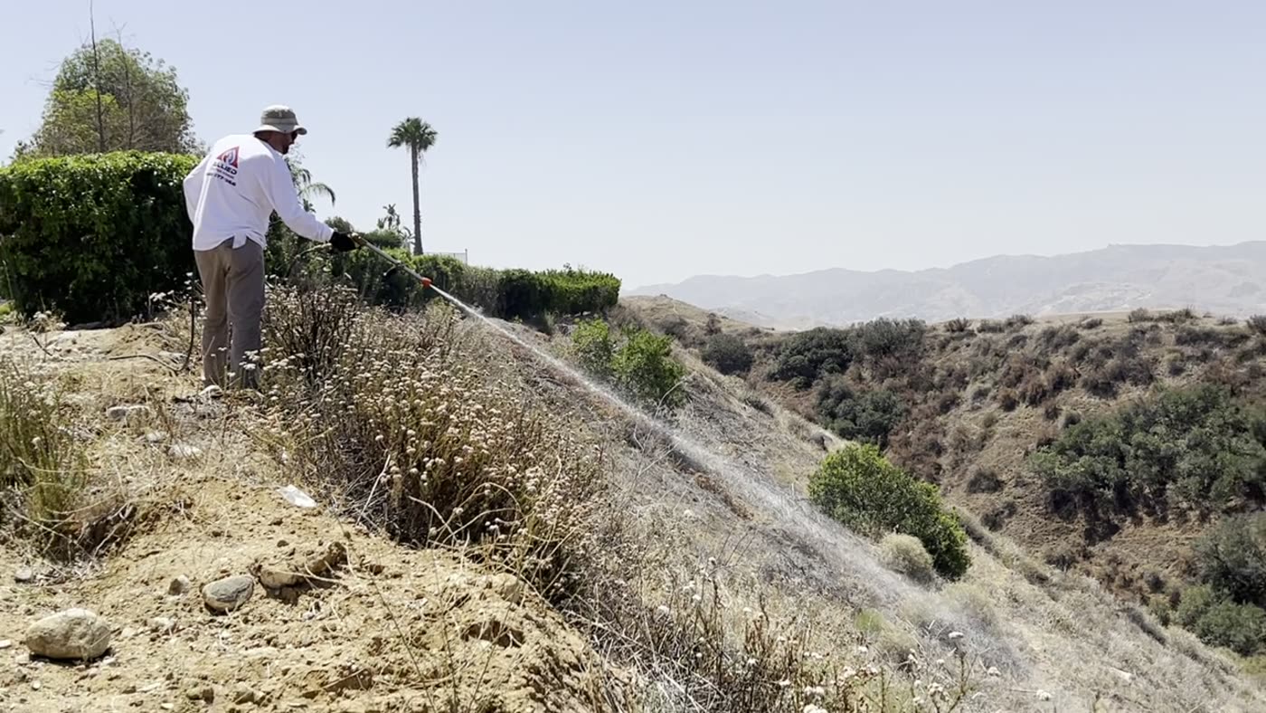 An Allied crew member applying long-term retardant across a hillside below an estate